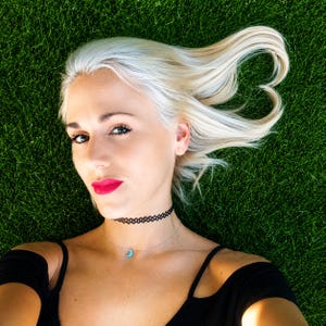 Lifestyle photo of a woman lying on green grass wearing a dainty moon opal necklace on a delicate chain with a black top and soft natural outdoor styling. lucky charms usa