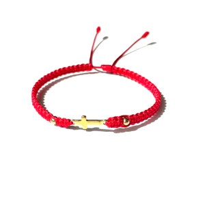May include: Red string bracelet with a gold cross charm and gold beads.