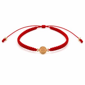 May include: A red braided cord bracelet featuring a central circular gold-toned charm with embossed religious iconography. The bracelet includes adjustable sliding knots and two small gold-toned beads at the ends of the cord strings.