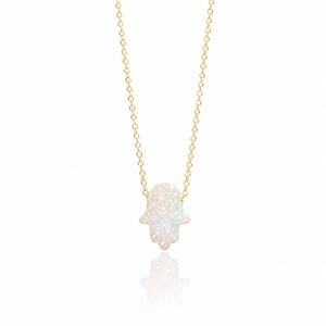 May include: A delicate gold chain necklace featuring a small, iridescent white opal-style hamsa hand pendant. The pendant displays a shimmering, multi-colored surface with flecks of pink, blue, and green light, suspended from a thin gold link chain.