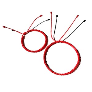 May include: Two red string bracelets, one larger than the other, are tied together. The bracelets are made of a braided red cord.