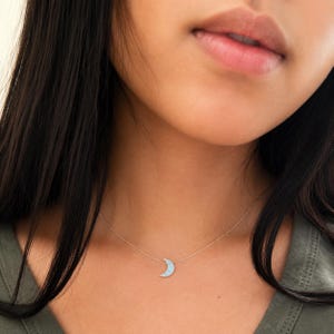 Close-up lifestyle photo of a woman with dark hair wearing a lucky charms usa dainty blue opal crescent moon necklace on a delicate chain with soft natural lighting and minimal everyday styling.