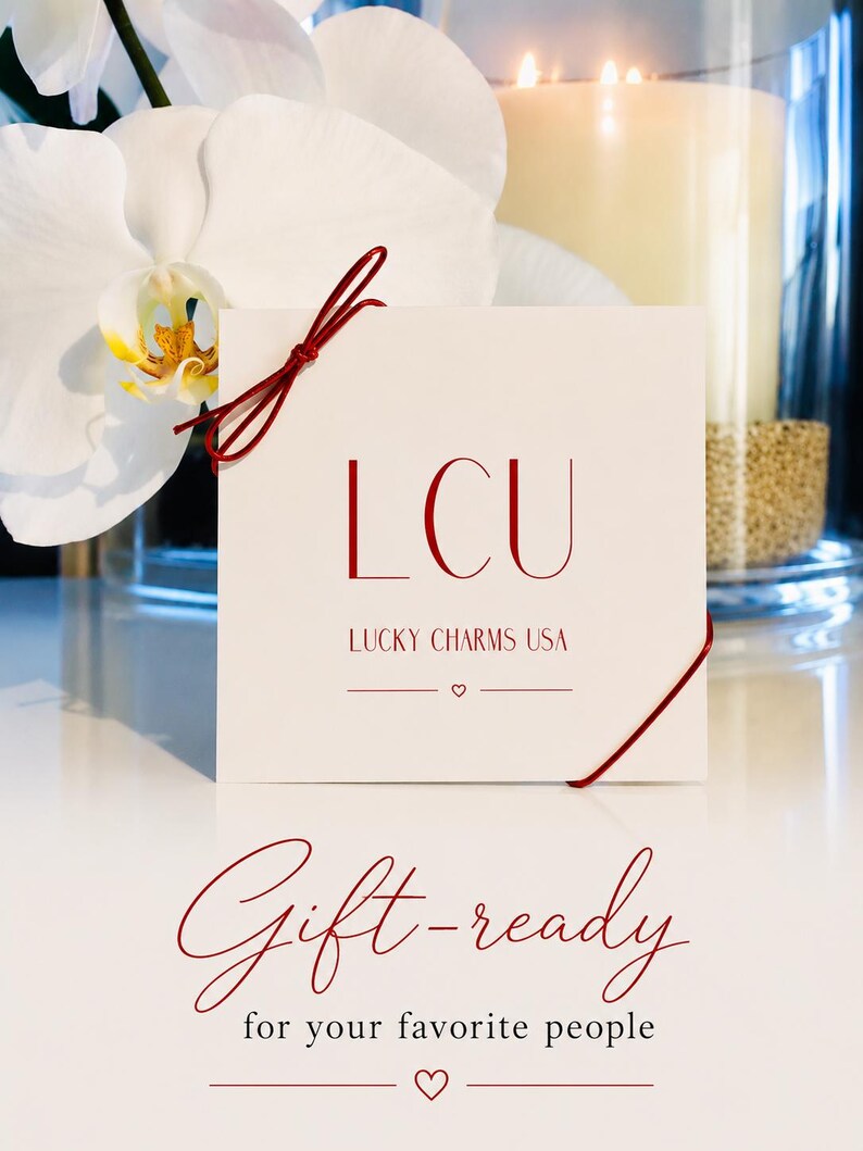 May include: A square white card with red text reading LCU LUCKY CHARMS USA and a small heart symbol. The card is tied with a thin red string and features the red script text Gift-ready for your favorite people with a small heart symbol below.