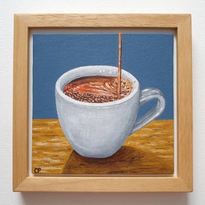 May include: A square painting in a wooden frame depicts a white coffee cup being filled with brown liquid. The background is blue, and the surface beneath the cup is a warm yellow-brown. The artist's initials, "CP," are in the lower left corner.