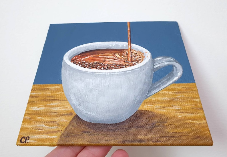 May include: A painting of a white coffee cup with a handle, filled with brown liquid, with a stream of coffee pouring into it. The background is blue and the surface is a light brown color. The painting is on a square canvas.