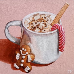 May include: A white mug filled with hot chocolate topped with marshmallows and a candy cane. A gingerbread man cookie sits next to the mug. The background is a light pink.