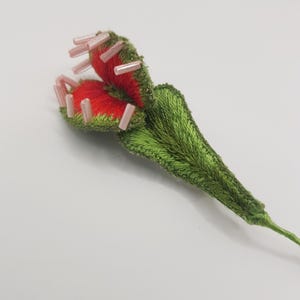 May include: Embroidered Venus flytrap with a red interior and green exterior. The plant features pink bead accents and detailed stitching. The leaves are a vibrant green, and the stem is a matching green.