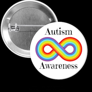 Può includere: Un bottone bianco con il testo "Autism Awareness" e un simbolo di infinito arcobaleno. Il bottone ha un retro argentato.