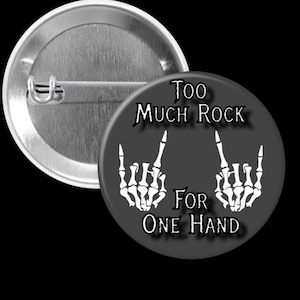 May include: A black and white button with the text "Too Much Rock For One Hand" and two skeleton hands making the rock and roll hand gesture.