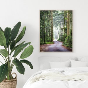 Puede incluir: Una impresi&oacute;n enmarcada que muestra un camino sinuoso a trav&eacute;s de un exuberante bosque verde. Altos &aacute;rboles bordean el camino, con la luz del sol filtr&aacute;ndose a trav&eacute;s del dosel. La impresi&oacute;n se muestra sobre una cama blanca.