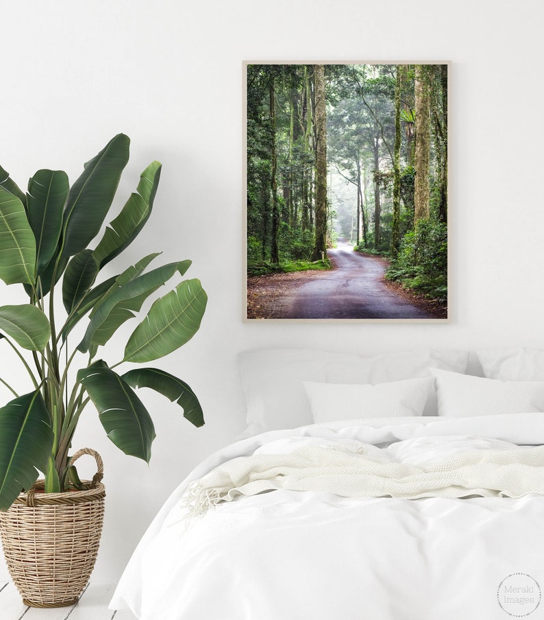 Puede incluir: Una impresi&oacute;n enmarcada que muestra un camino sinuoso a trav&eacute;s de un exuberante bosque verde. Altos &aacute;rboles bordean el camino, con la luz del sol filtr&aacute;ndose a trav&eacute;s del dosel. La impresi&oacute;n se muestra sobre una cama blanca.