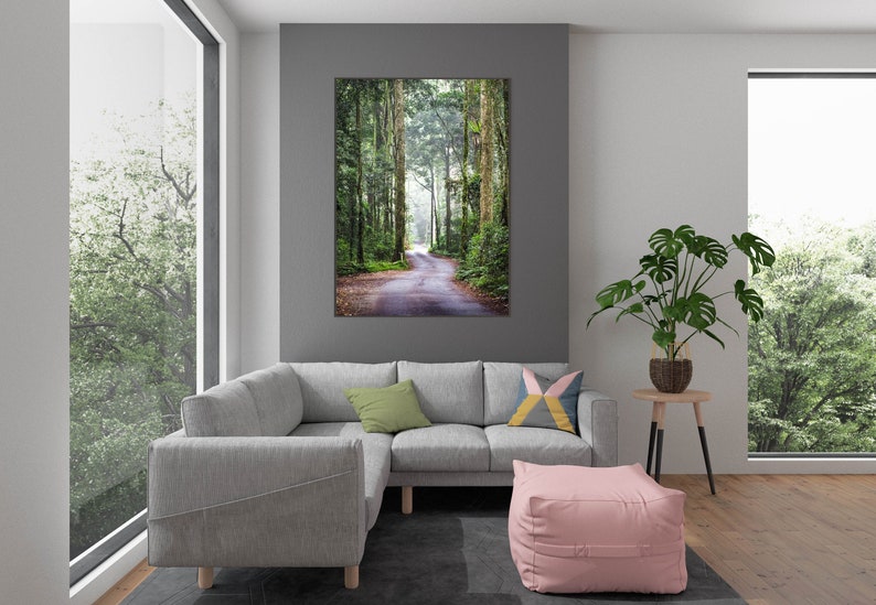 Puede incluir: Un cuadro enmarcado de una carretera que serpentea por un exuberante bosque verde cuelga de una pared gris. Un sof&aacute; seccional gris, un puf rosa y una planta en maceta est&aacute;n frente a una gran ventana.