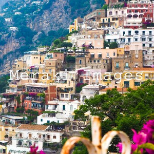 Puede incluir: Una vista pintoresca de un pueblo costero en una ladera. Edificios con fachadas coloridas en tonos amarillos, rosas y blancos descienden en cascada por la ladera. Frondosos &aacute;rboles verdes y vibrantes flores rosas enmarcan el primer plano. Incluye el texto "Meraki Images".