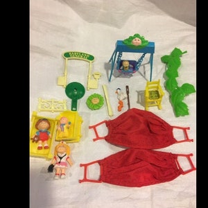 May include: A set of plastic toys for children, including a swing set, a slide, a sandbox, and two dolls. The toys are in various colours, including green, yellow, blue, and red.