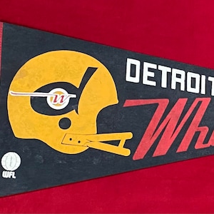 May include: A black and red pennant with the words "DETROIT WHEELS" in red and white lettering. A yellow and black football helmet is on the left side of the pennant. The WFL logo is in the lower left corner.