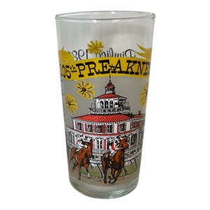 May include: A clear glass with a frosted background featuring a colorful illustration of a horse race and a building with a red roof. The text "105th PREAKNESS" is displayed in yellow. Yellow flower illustrations are also present.