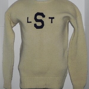 May include: A cream-colored knitted sweater with a navy blue "S" and the letters "LST" on the front.