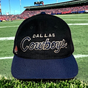 May include: A black and navy blue baseball cap with the words "Dallas Cowboys" in gold lettering.