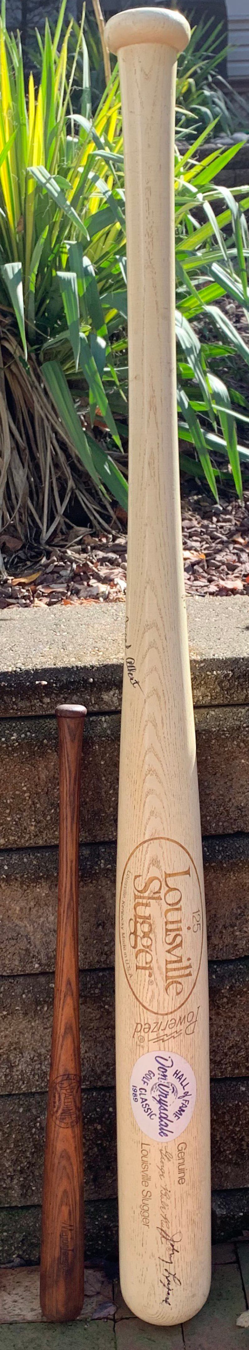 May include: A wooden Louisville Slugger baseball bat with a white label that reads "Genuine Louisville Slugger" and "Hall of Fame Don Drysdale Golf Classic 1989". The bat is 125 cm long and has a brown wooden handle.