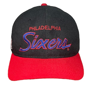 May include: Black and red baseball cap with the words "Philadelphia Sixers" embroidered in blue and red on the front.