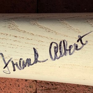 May include: A white wooden baseball bat with a black signature that reads "Frank Albert".