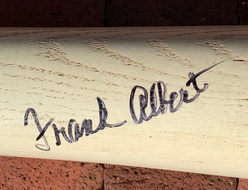 May include: A white wooden baseball bat with a black signature that reads "Frank Albert".