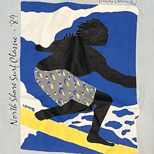 May include: A blue and white illustration of a surfer riding a wave. The surfer is silhouetted in black and wearing grey shorts with a white and yellow pattern. The text "North Shore Surf Classic - '89" is on the left side of the image and "Harvey Cedars, N.J." is on the top right. The text "Mayetta Beach c 1989" is at the bottom right.