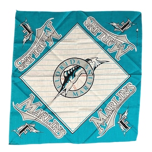 May include: A square, turquoise bandana featuring the Florida Marlins logo. The center diamond has the team logo and pinstripes. The word "Marlins" is printed in gray and white on each side of the bandana. The bandana is made of a soft fabric.