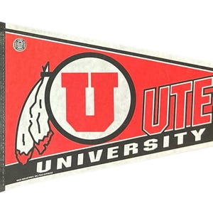 May include: A red, white, and black pennant with the text "UTES UNIVERSITY OF UTAH". The pennant features a large red "U" inside a white circle, and a Native American headdress graphic. The pennant is made of felt.