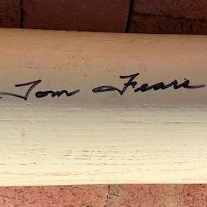 May include: White wooden baseball bat with black ink signature "Tom Seaver" on the surface.
