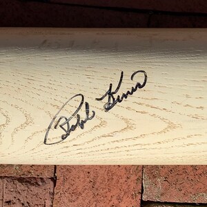 May include: A white wooden baseball bat with a black signature that reads "Bobbi Brown".