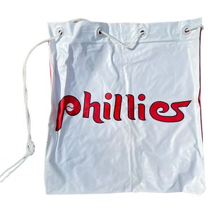 May include: White drawstring bag with a red "Phillies" logo. The bag has a white drawstring and is made of a lightweight material.