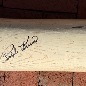 May include: A white wooden baseball bat with black signatures from Eddie Murray, Bob Feller, and Tom Seaver.