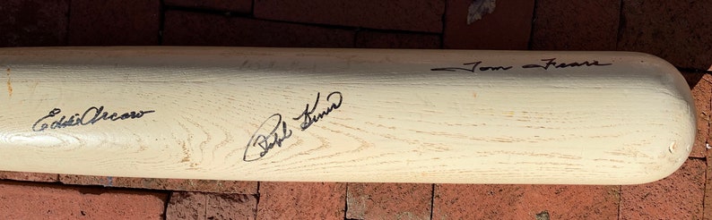 May include: A white wooden baseball bat with black signatures from Eddie Murray, Bob Feller, and Tom Seaver.