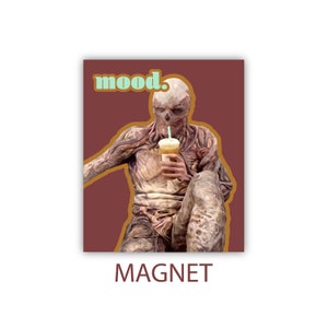 May include: A brown and gold magnet with a cartoon image of a monster holding a cup of coffee with a straw. The text "mood." is in light blue on the magnet.