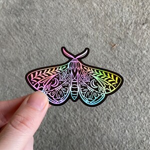 May include: A rainbow iridescent sticker of a moth with intricate floral and moon designs.