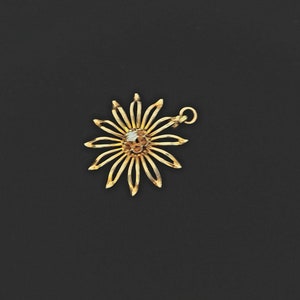 May include: A gold flower charm with a single white diamond in the centre. The charm has a loop at the top for attaching to a necklace or bracelet.