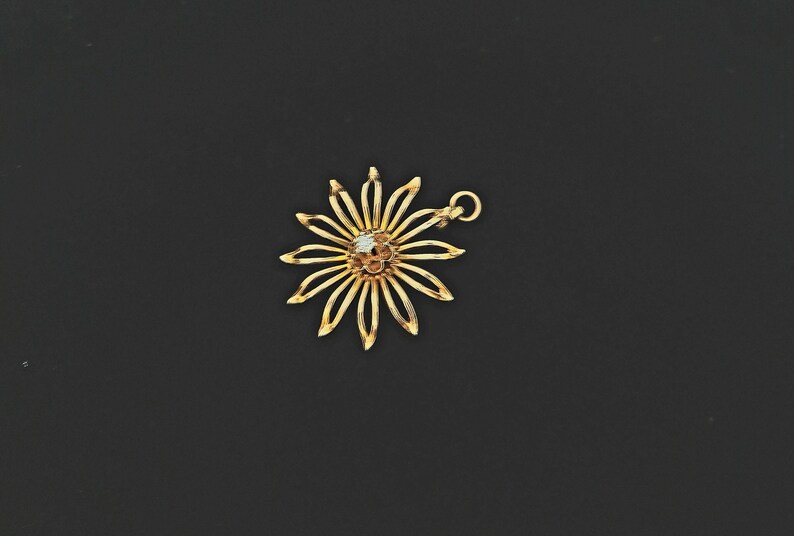 May include: A gold flower charm with a single white diamond in the centre. The charm has a loop at the top for attaching to a necklace or bracelet.
