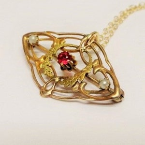 Puede incluir: Un collar de oro con un delicado diseño de filigrana que presenta una piedra preciosa roja y dos perlas blancas.