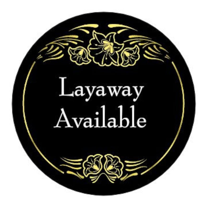 May include: Black and gold circular sign with a decorative floral border. The sign reads "Layaway Available" in white text.