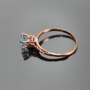 K&ouml;nnte beinhalten: Ein Ring aus Ros&eacute;gold mit einem hellblauen Edelstein, der in einem filigranen Design gefasst ist.