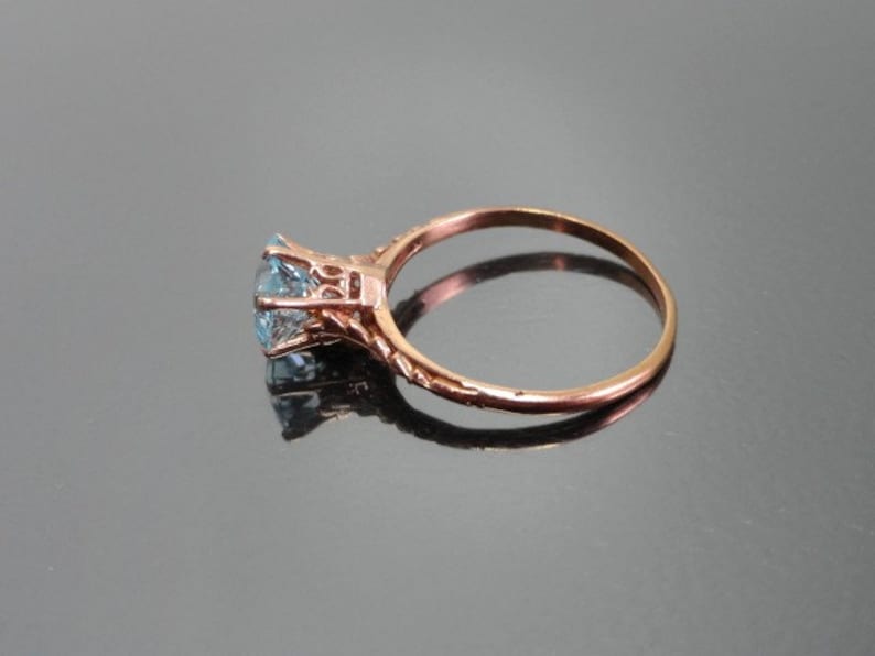 K&ouml;nnte beinhalten: Ein Ring aus Ros&eacute;gold mit einem hellblauen Edelstein, der in einem filigranen Design gefasst ist.