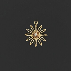 May include: A gold-toned pendant in the shape of a flower with a single clear gemstone in the centre.