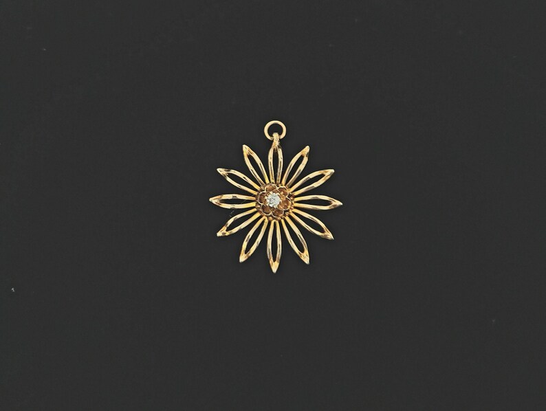 May include: A gold-toned pendant in the shape of a flower with a single clear gemstone in the centre.
