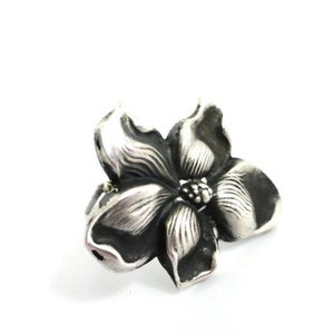 Puede incluir: Un anillo de plata con un dise&ntilde;o de flor detallado. La flor tiene cinco p&eacute;talos y un centro con un peque&ntilde;o c&iacute;rculo en relieve.