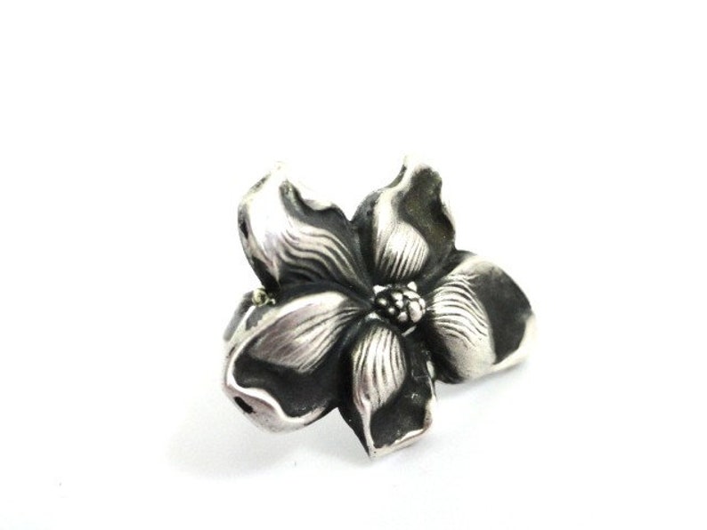 Puede incluir: Un anillo de plata con un dise&ntilde;o de flor detallado. La flor tiene cinco p&eacute;talos y un centro con un peque&ntilde;o c&iacute;rculo en relieve.