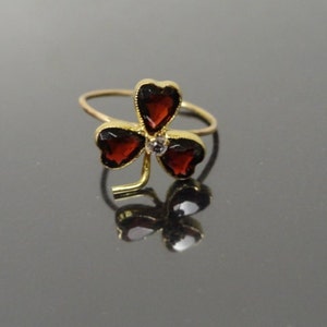May include: A gold ring with a three-leaf clover design. Each leaf is set with a red gemstone, and a smaller white gemstone is in the center.