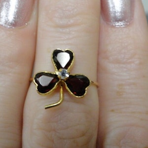 May include: A gold ring with a four-leaf clover design. The clover is made of red gemstones and a single white gemstone in the center.