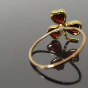 May include: A gold ring with a red clover design. The clover is made of four leaves with red gemstones in the center of each leaf.