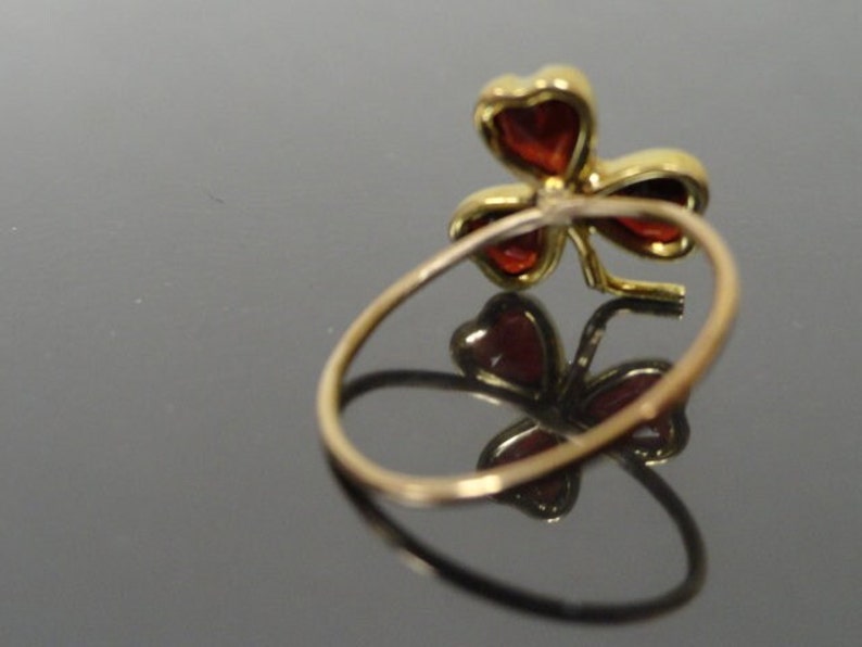 May include: A gold ring with a red clover design. The clover is made of four leaves with red gemstones in the center of each leaf.